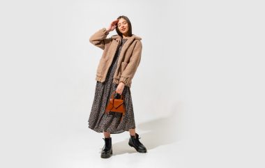 Lovely european model in stylish fur coat and dress . Wearing  ankle boot in black leather. Holding  brown handbag.