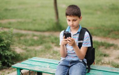 Young boy with backpack sitting on the bench and play online games during school break.